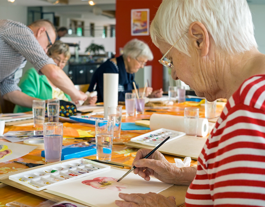 Residents painting at a table during an art class in a communal area of a senior living community.