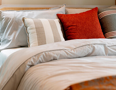 Cozy bed in a senior living unit with white and striped pillows and a burnt orange cushion.