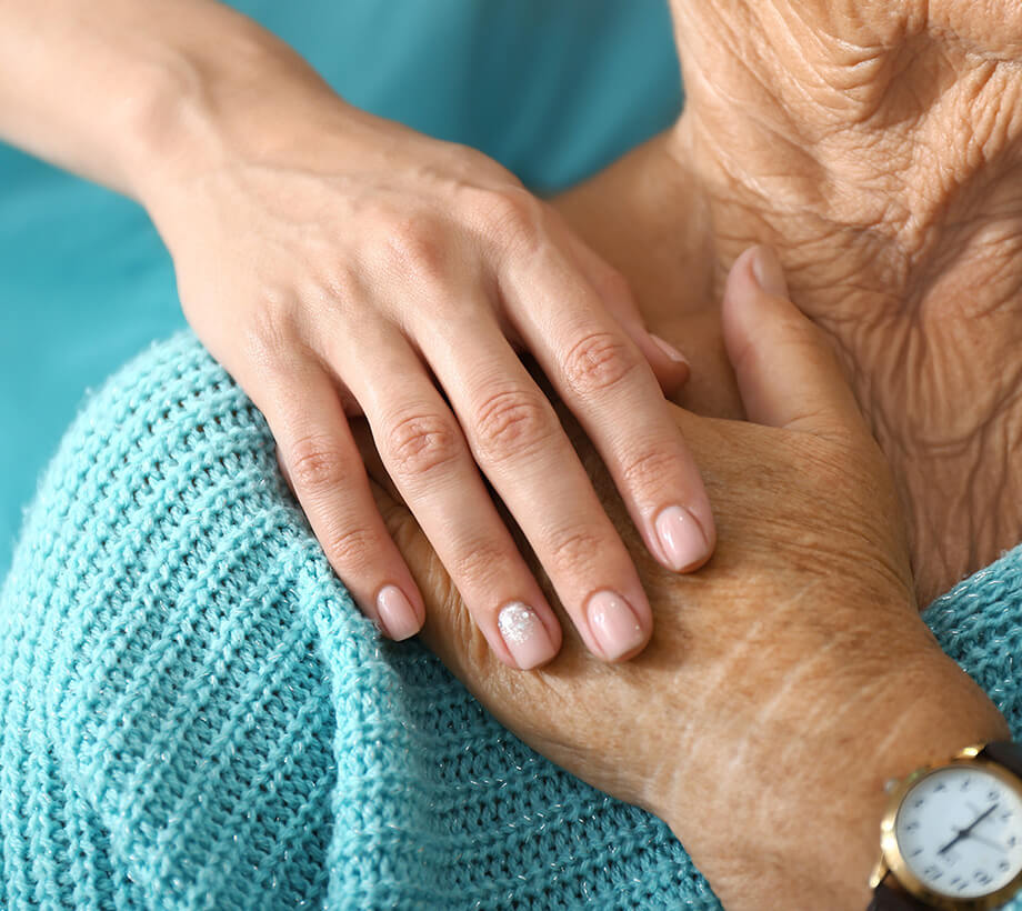 Close-up of a young hand reassuringly holding an elderly hand with a blue sweater and a watch.