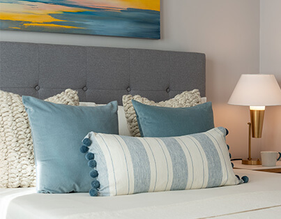 Comfortable bed with blue and white pillows, modern lamp, and abstract wall art in a cozy unit.