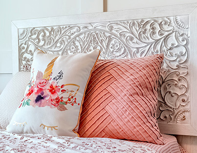 Close-up of a decorative carved headboard and two accent pillows on a bed in a living unit.