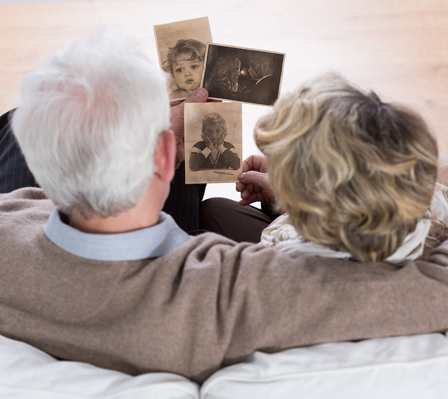 Elderly couple sitting on a couch looking at old black and white family photographs.