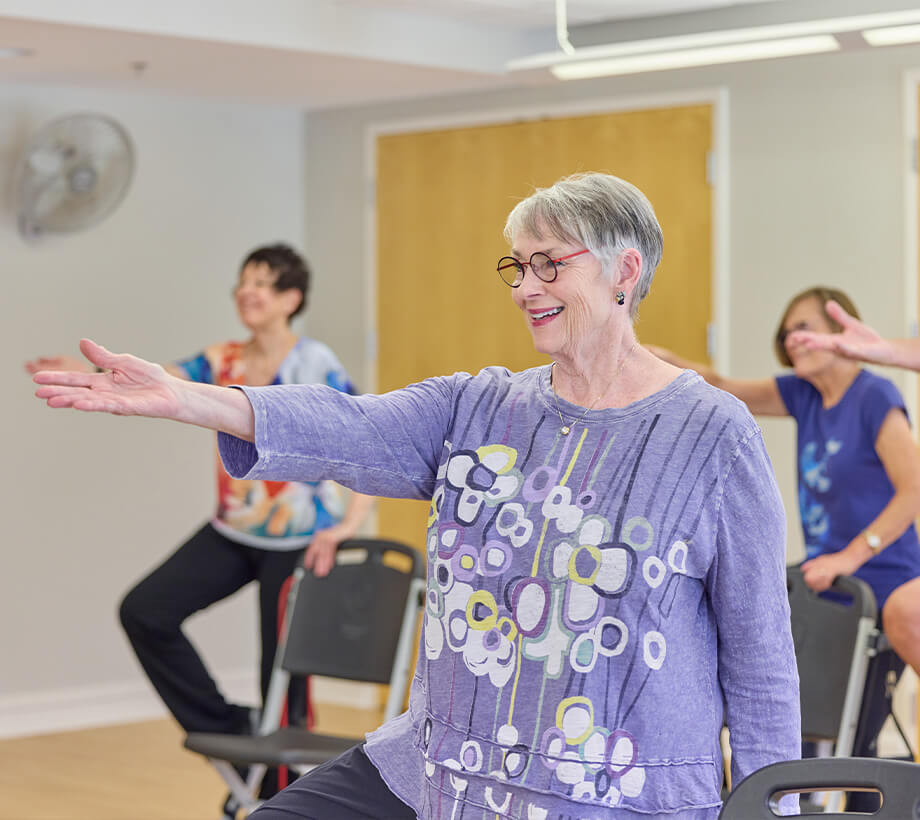 Residents participating in group exercise class at senior living community, smiling and active.