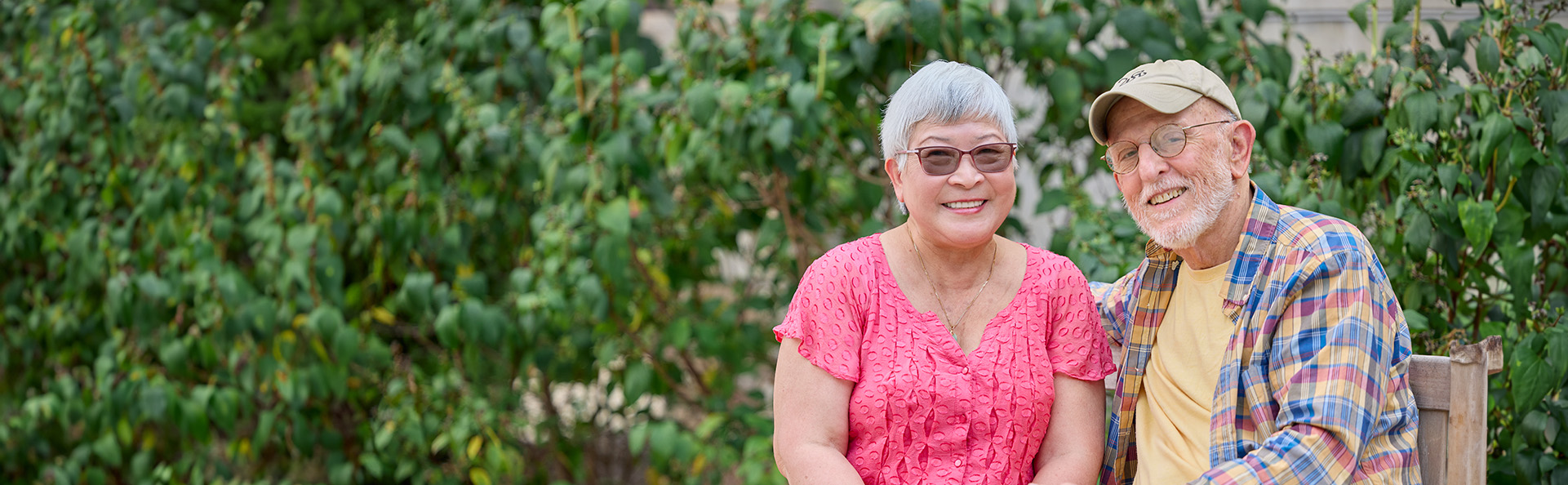 Senior couple sitting on a bench and smiling in a garden at a senior living community.