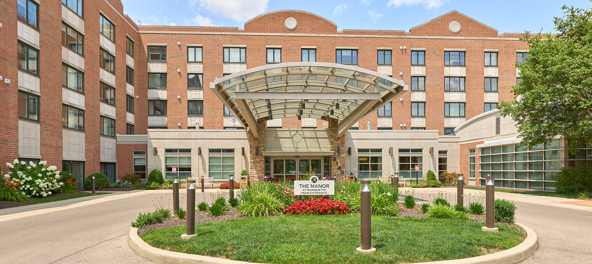 Main entrance of The Manor at Marquette with a van parked under the covered canopy.