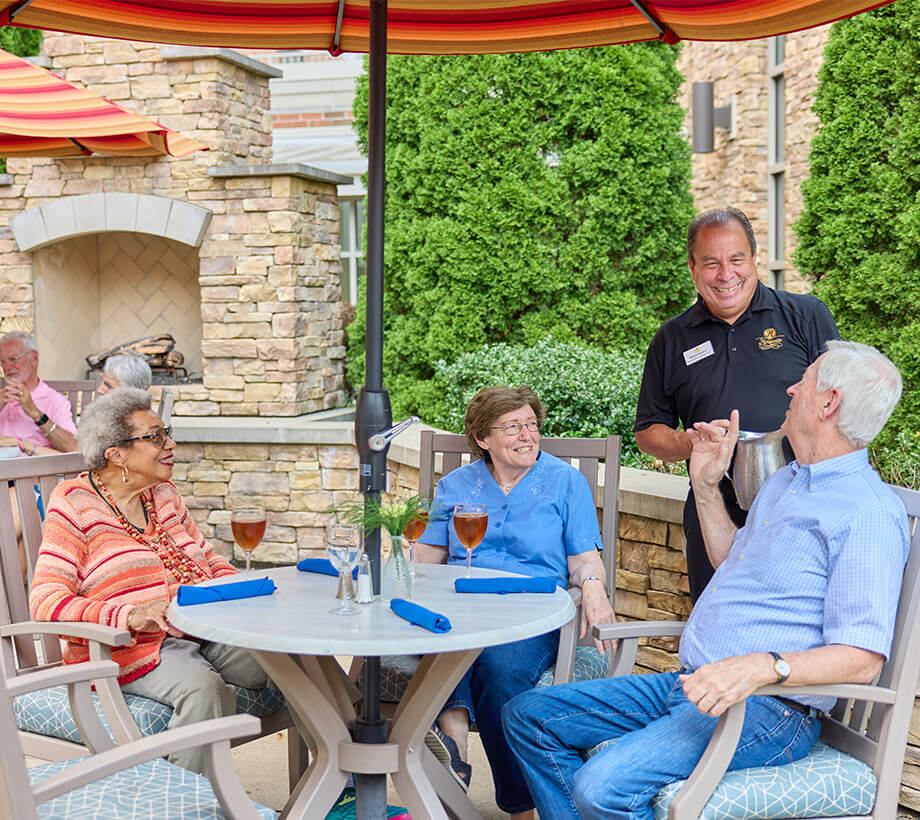 Residents enjoying drinks and conversation on outdoor patio with staff member standing by.