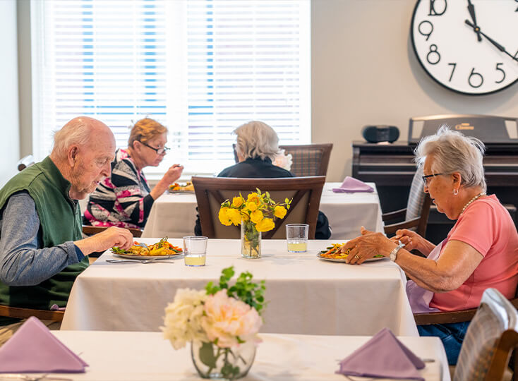 Seniors enjoying a meal in a communal dining area with white tablecloths and floral centerpieces.