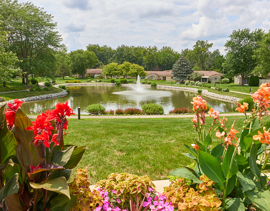 Beautiful garden view of a central pond with fountain surrounded by green lawns and units.