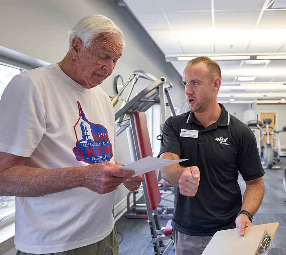 Senior man receiving exercise instruction from a fitness trainer in a gym at a senior living community.