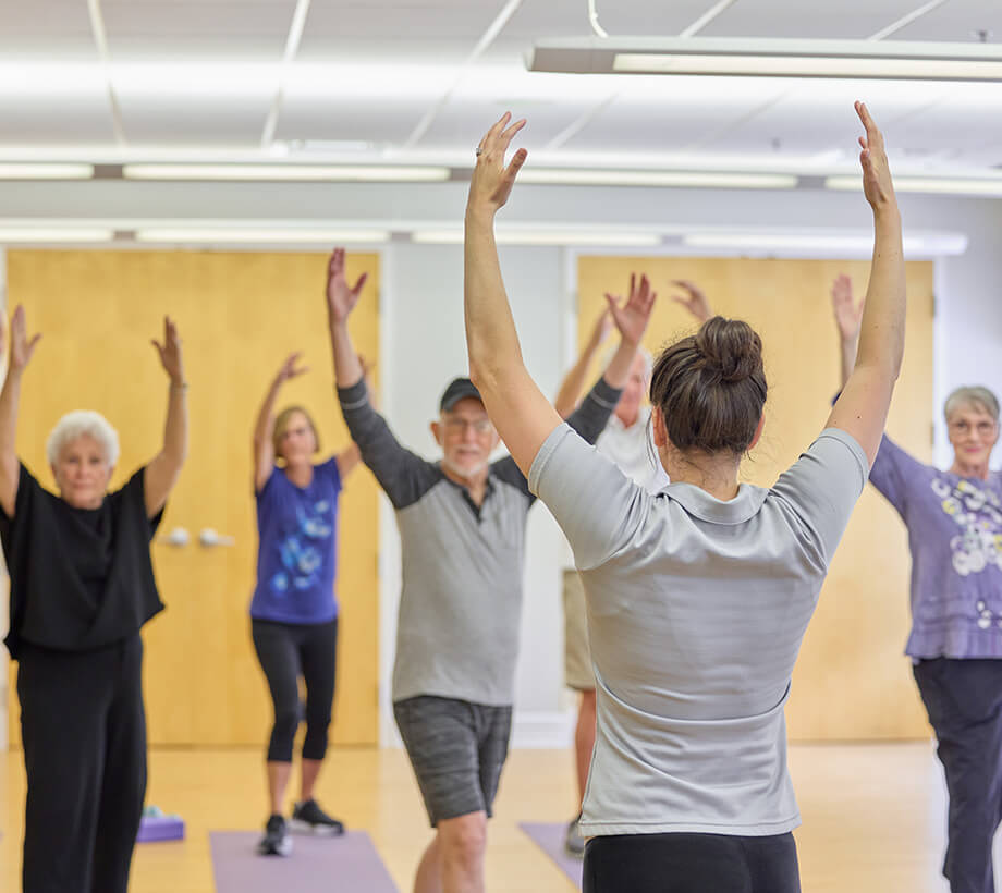 A fitness instructor leads a group of seniors in a stretching exercise routine in a community room.