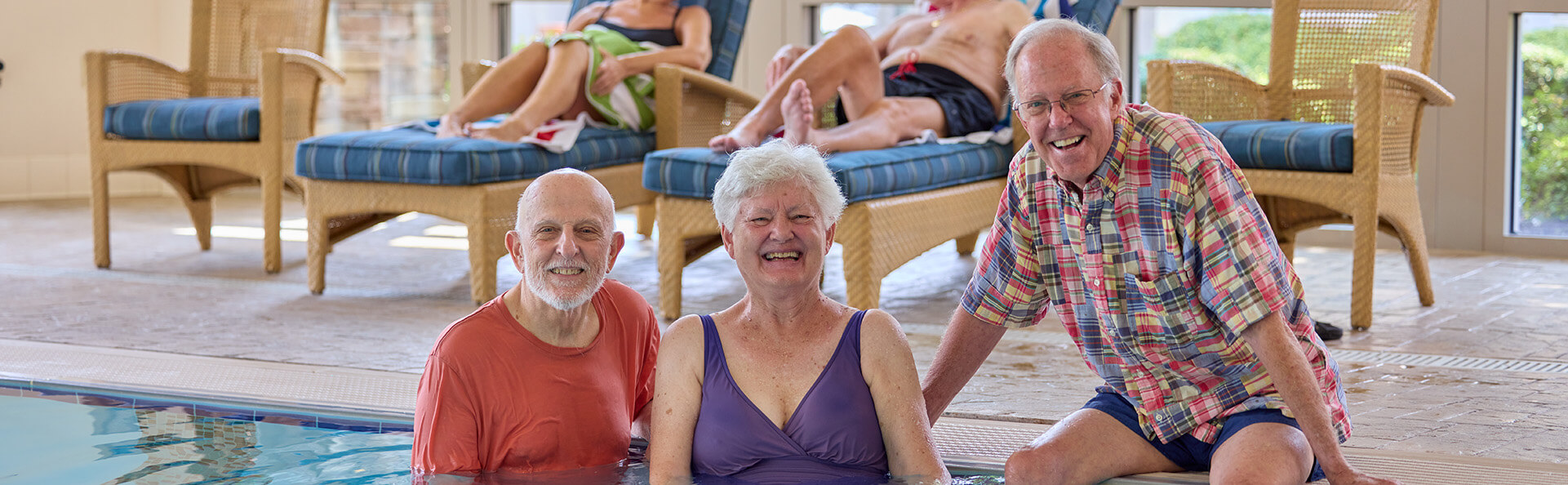 Three seniors by the edge of an indoor pool at a senior living rec center