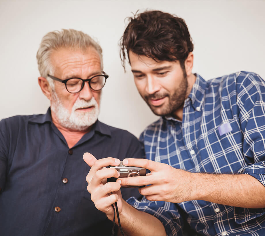 Elderly man and younger man examining a digital camera together in a bright room.