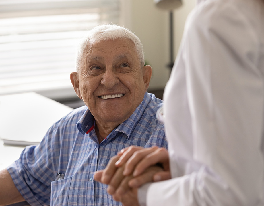 Smiling elderly man holding hands with a nurse in a senior living unit.