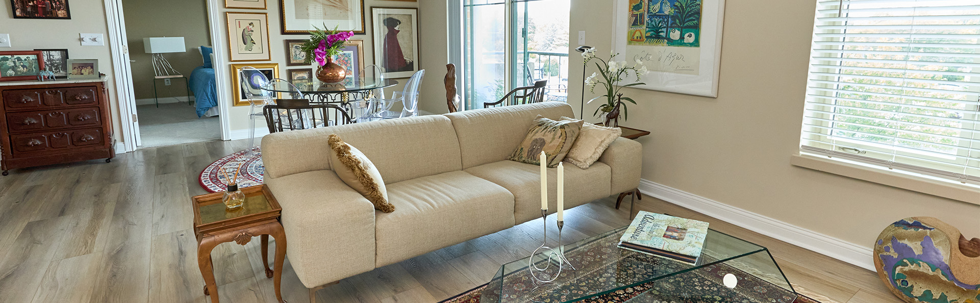 A bright living area with modern furniture, large artworks, and a glass-top coffee table.