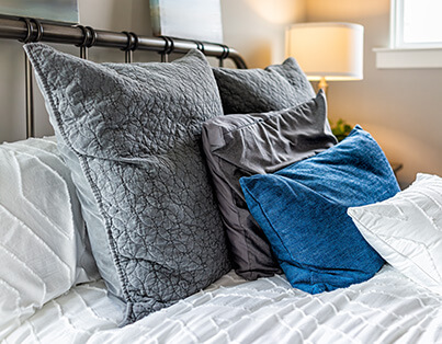 Comfortable bed with decorative pillows in a unit. A bedside lamp is turned on.